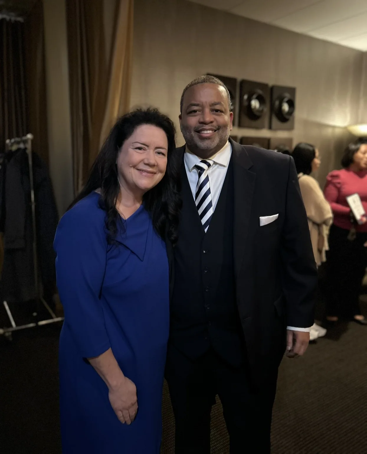 Smiling woman in blue dress and man in dark suit posing at a reception