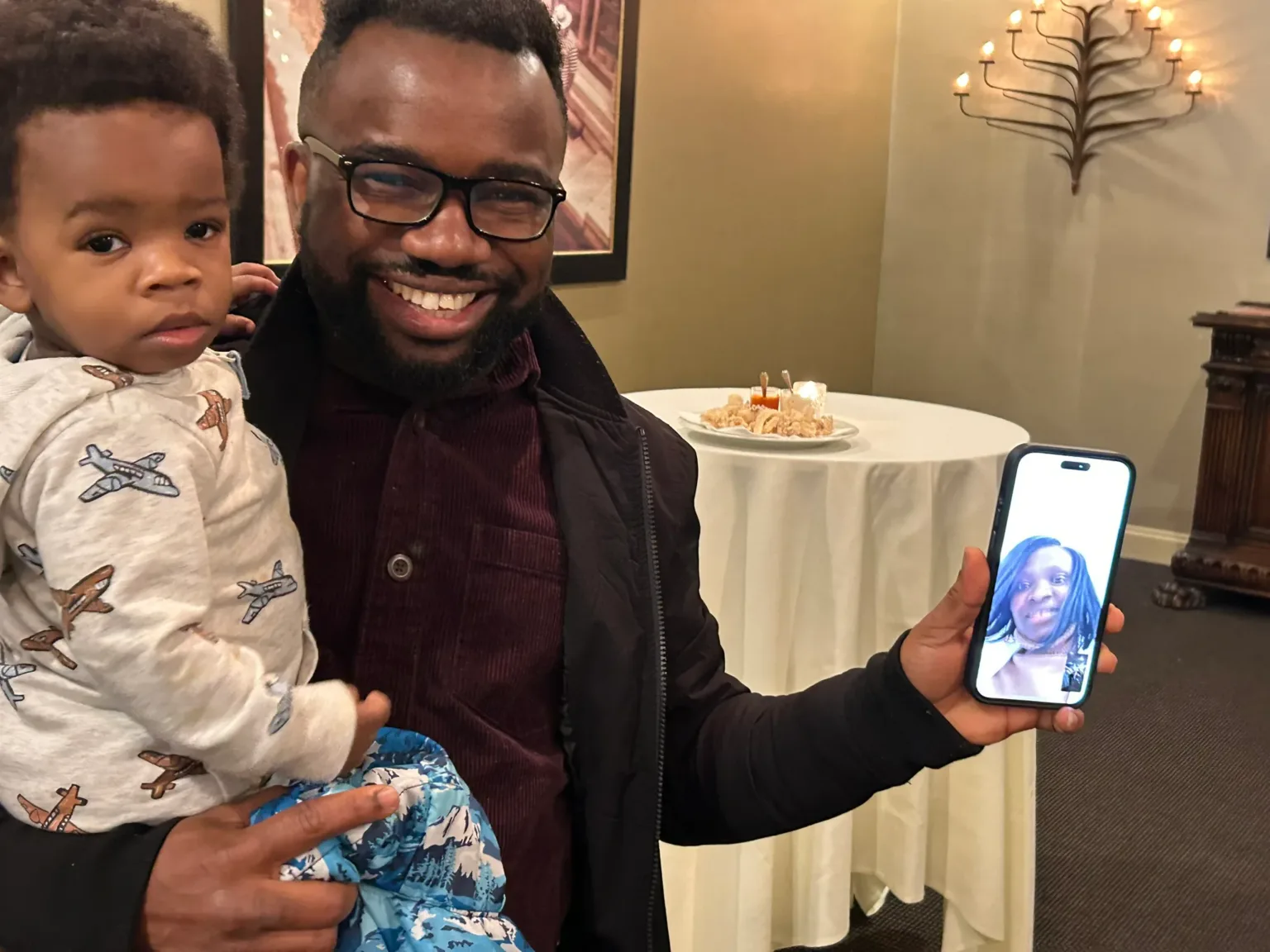 Smiling man holding a toddler and a phone showing a photo