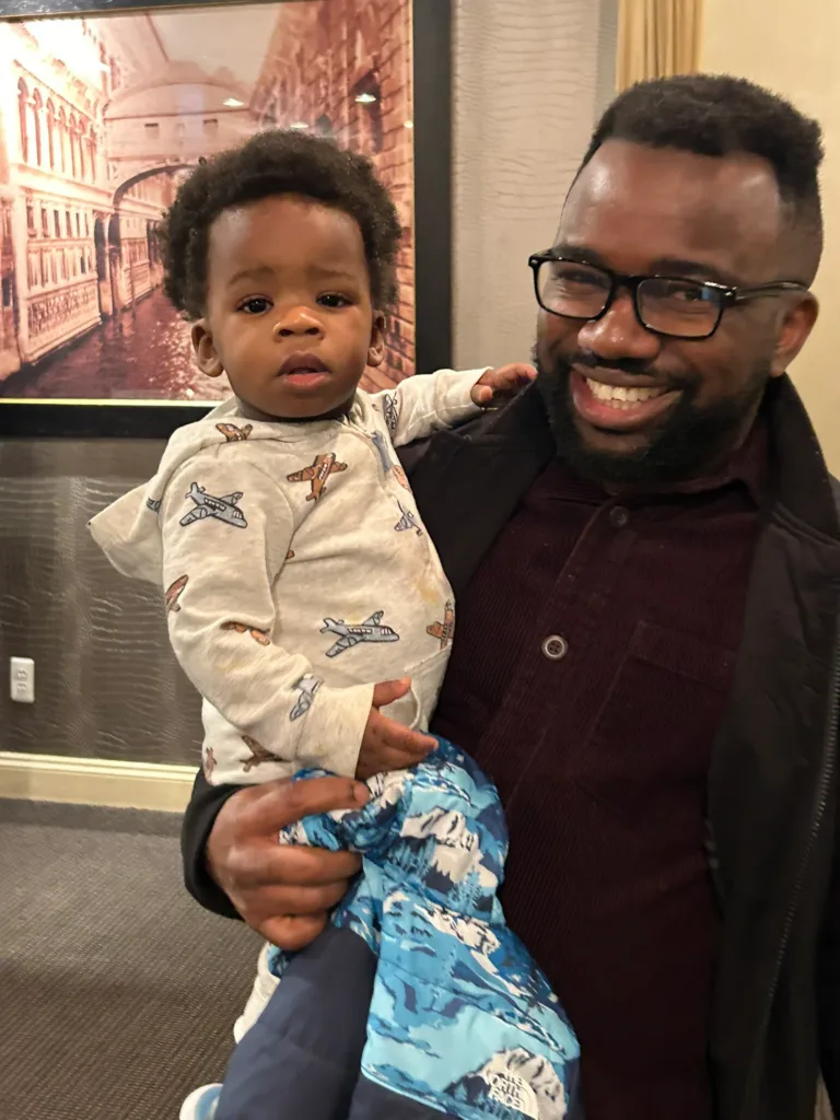 Smiling man in glasses holding a toddler in a blue blanket
