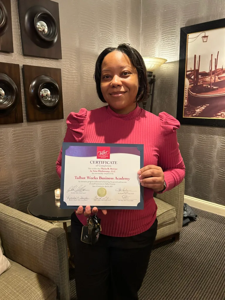 Woman in pink sweater holding a Talbot Works Business Academy certificate