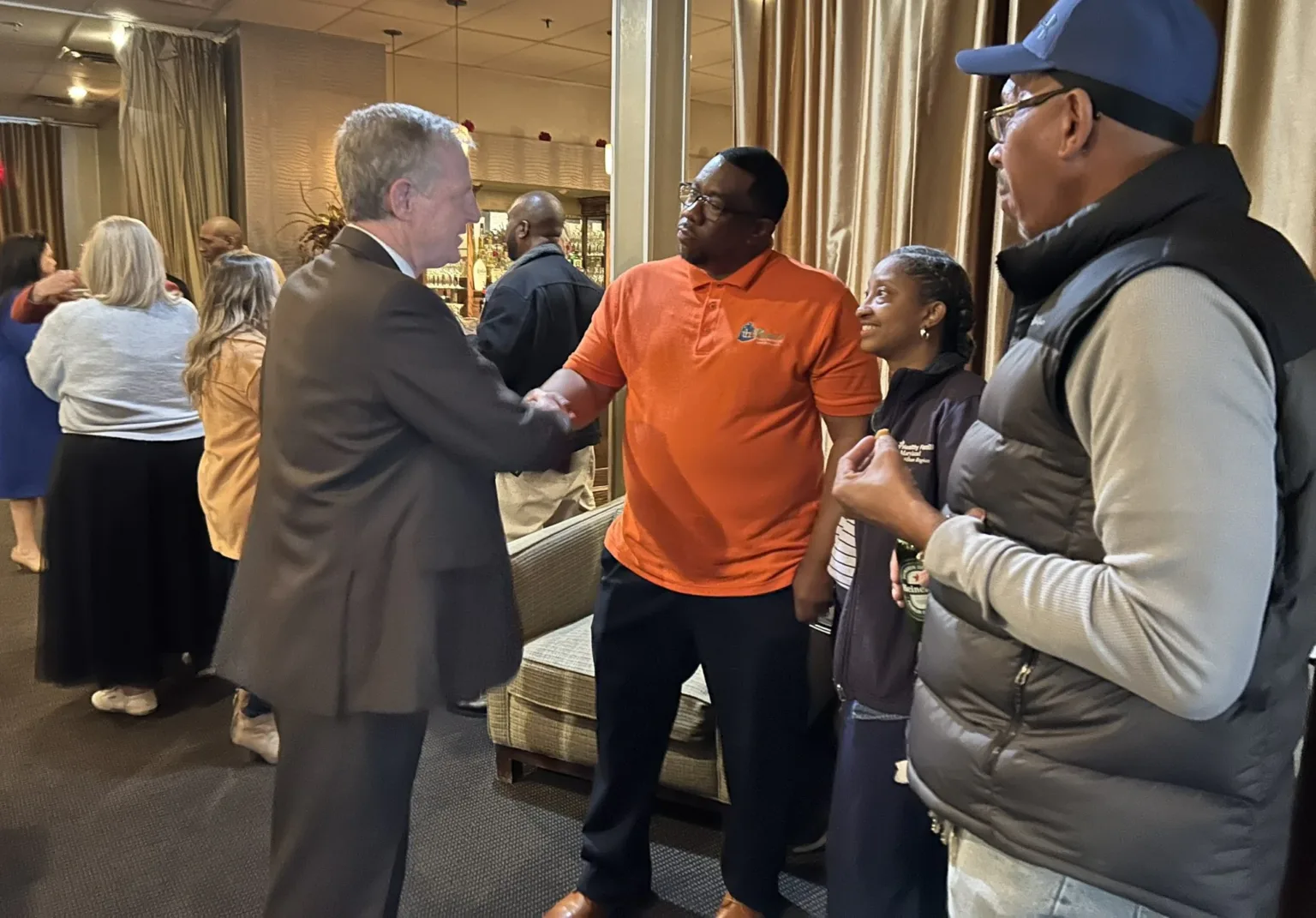 Man in suit greeting a man in orange shirt at a reception