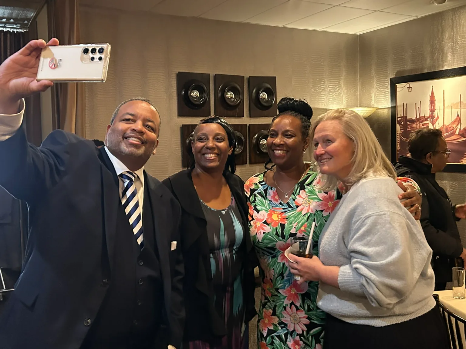 Four women and a man posing for a selfie at a reception