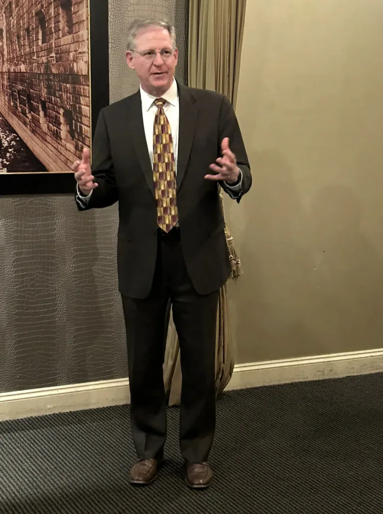 Man in tan suit gesturing while speaking at a reception
