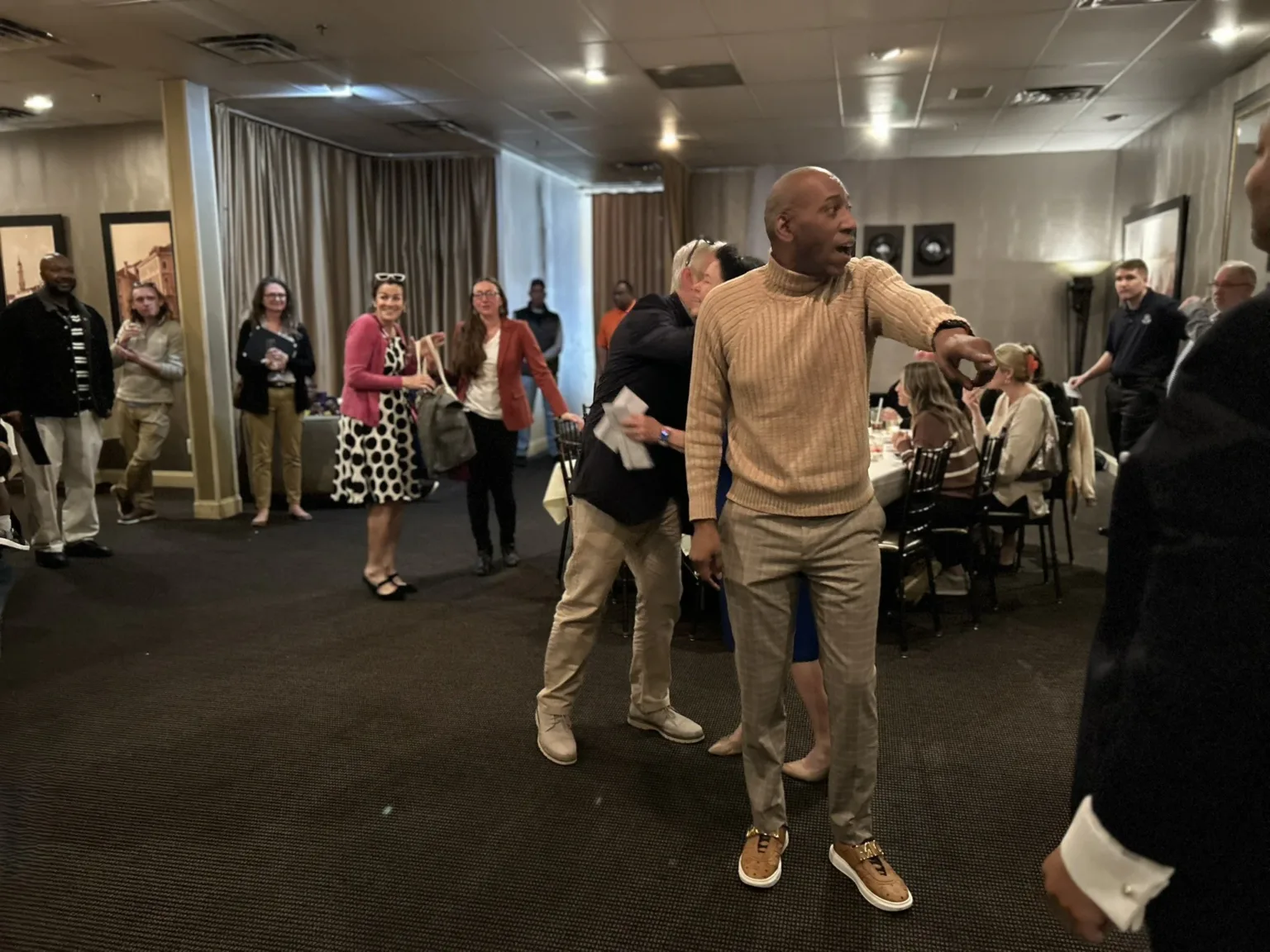 Man in tan sweater leading guests through a banquet room