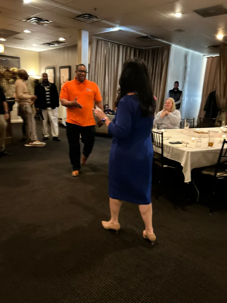 Man in orange polo and woman in blue dress walking through a reception room