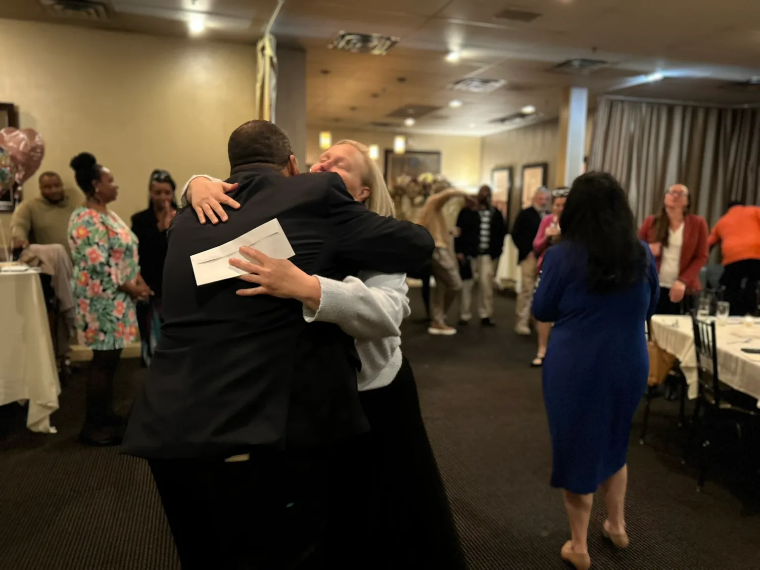 Two men embracing at a reception, guests in background