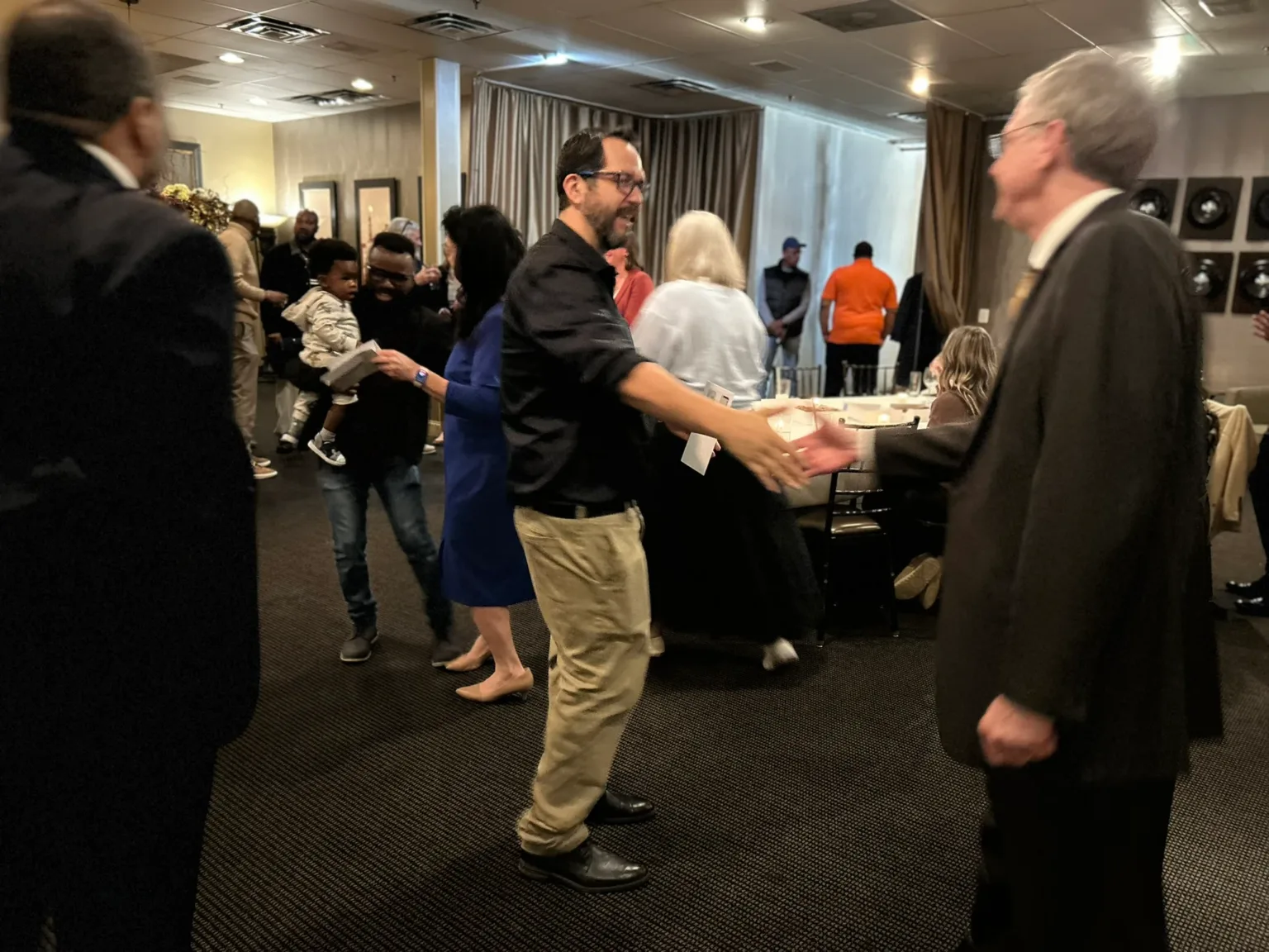 Men in dark jackets at a reception, one handing a plate to a guest