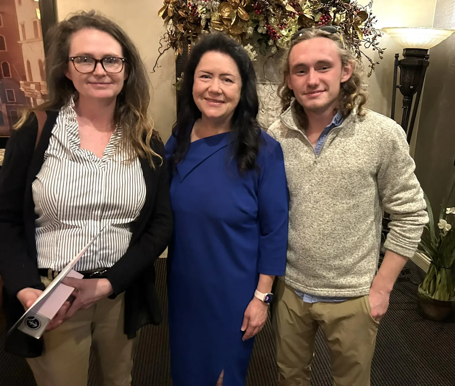Three guests posing at a reception: two women and a young man in a sweater