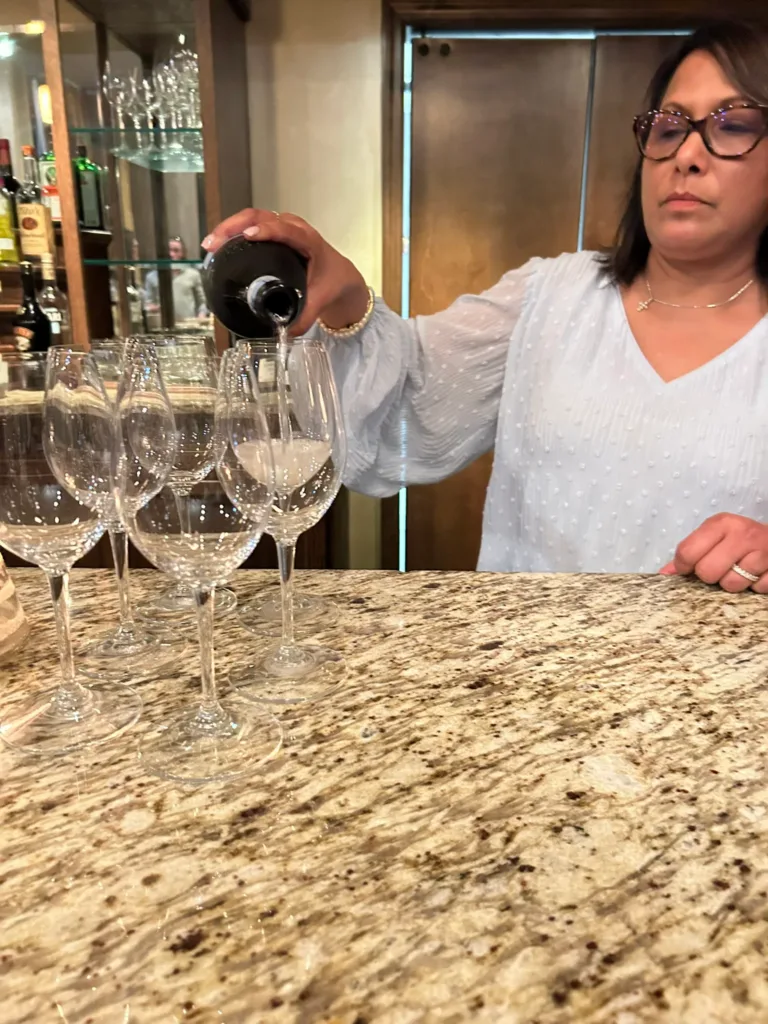 Woman in white top pouring wine into glasses on a granite counter