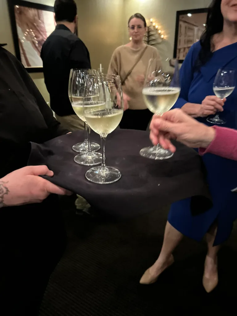 Tray of white wine glasses held by a server at a reception