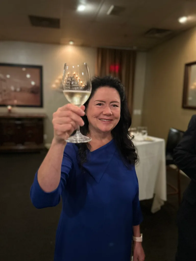 Woman in blue top raising a glass of white wine and smiling