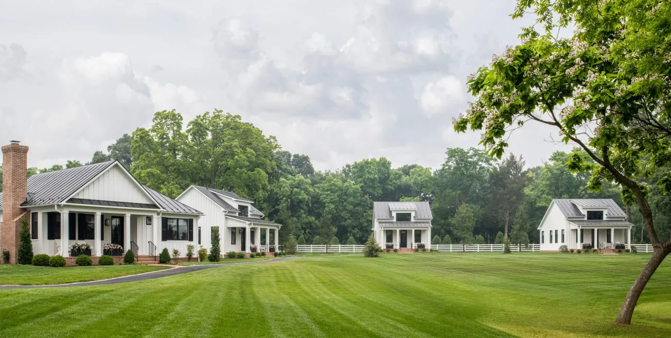 White farmhouse-style cottages with a manicured lawn and trees