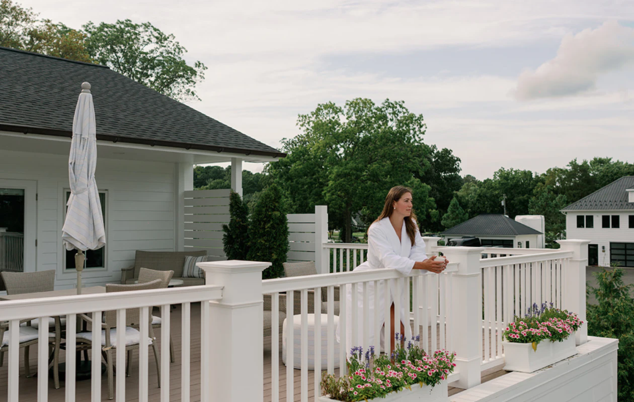 Woman on a white porch railing beside a cottage with flower boxes