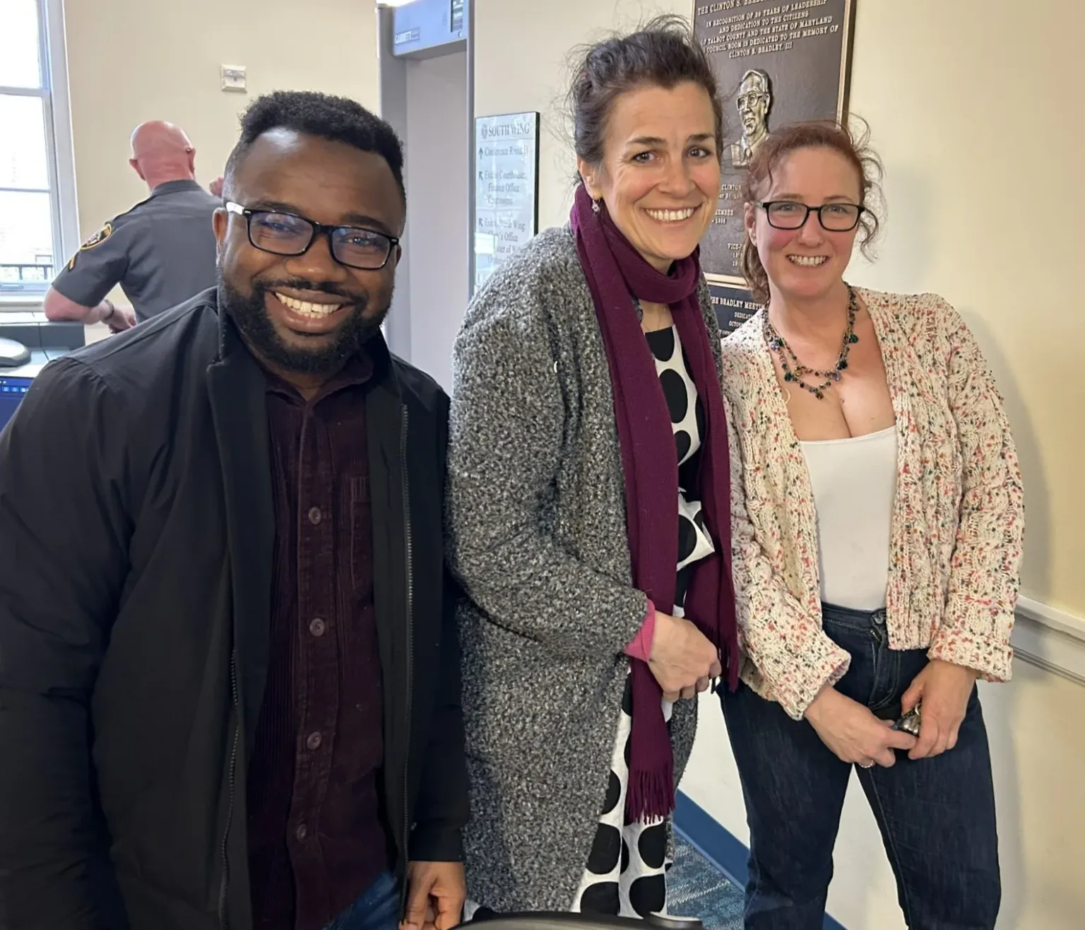 Three people smile together in an indoor hallway.