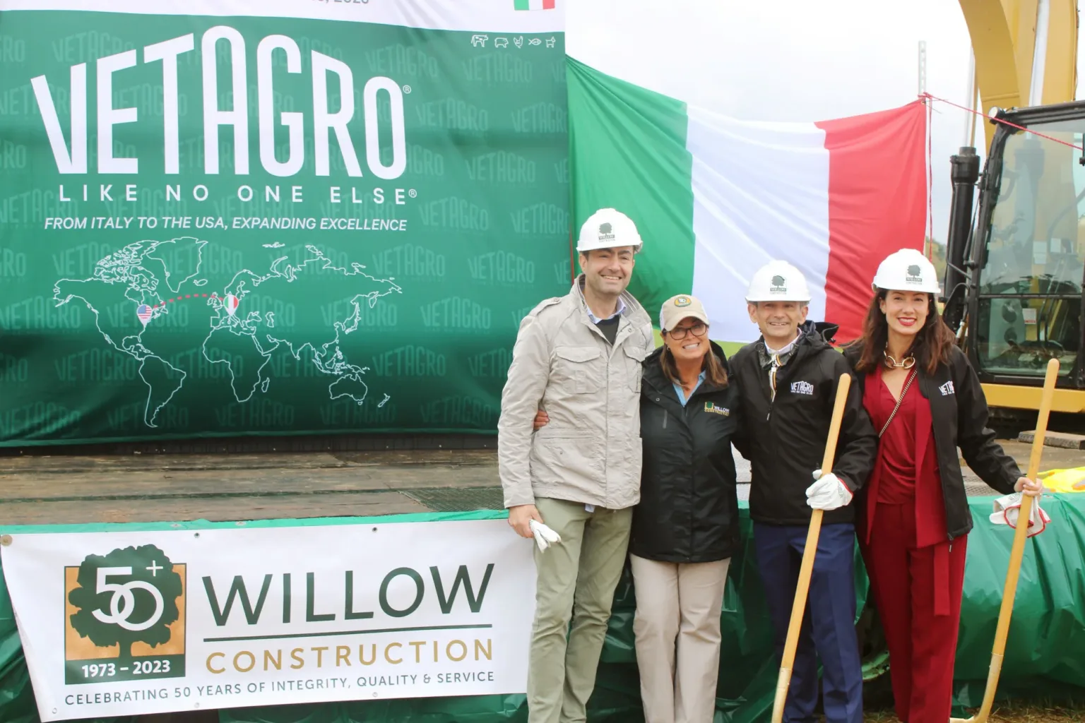 Four people in hard hats pose before a Vetagro banner and a Willow Construction sign.