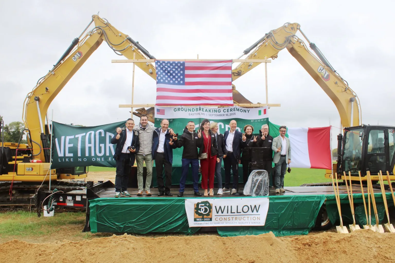 Groundbreaking crowd on a stage with excavators, an American flag, and a Vetagro banner.