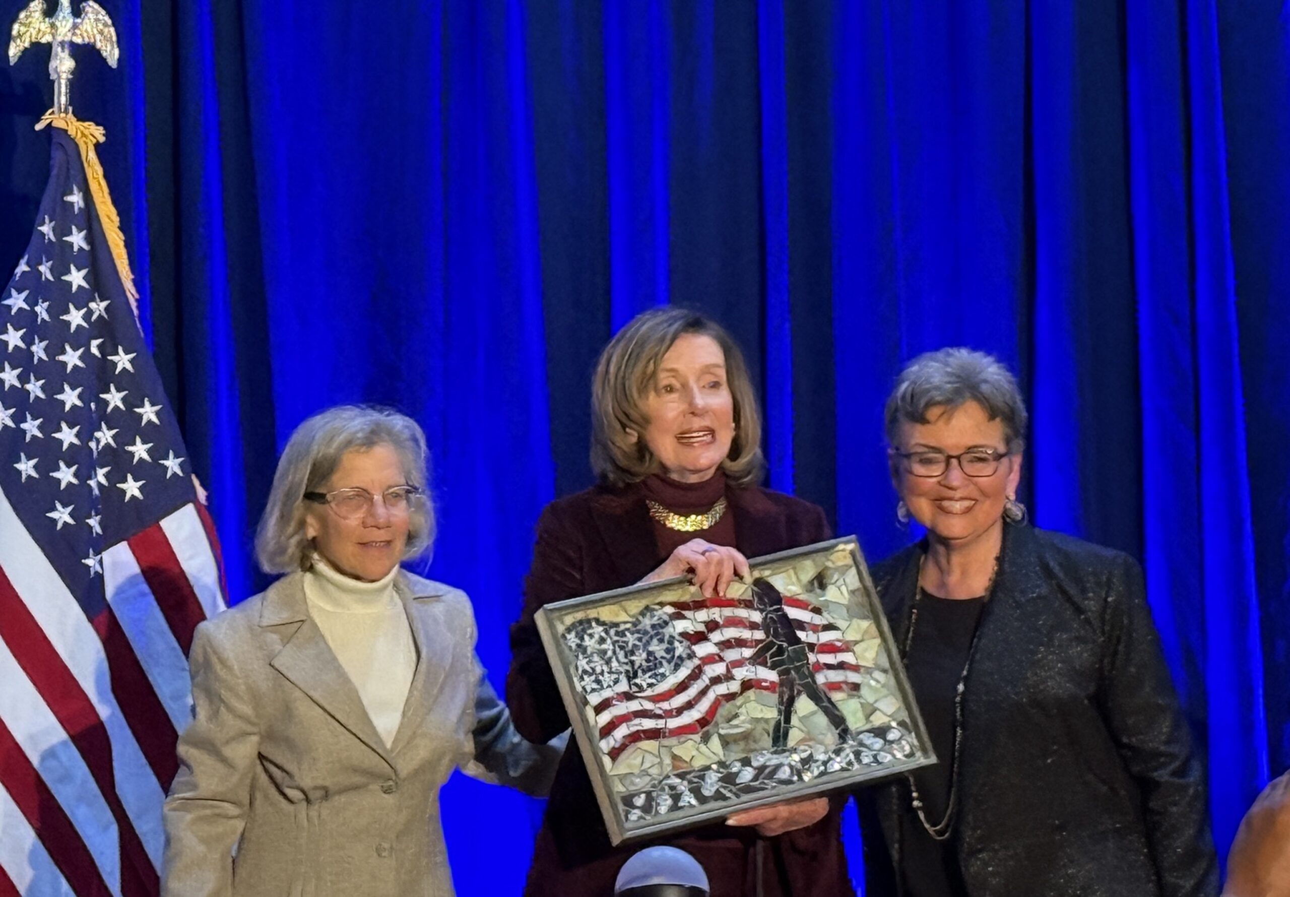 Nancy Pelosi, center, holds the mosaic artwork titled Shattered during a reception at Trinity Washington University. The piece, created by Maryland artist Jennifer Wagner, symbolizes resilience and breaking barriers.
