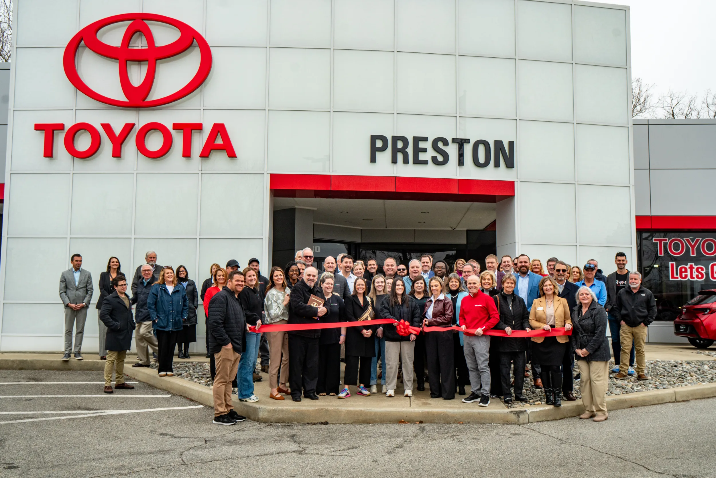 Large group behind a red ribbon in front of a Toyota dealership named Preston