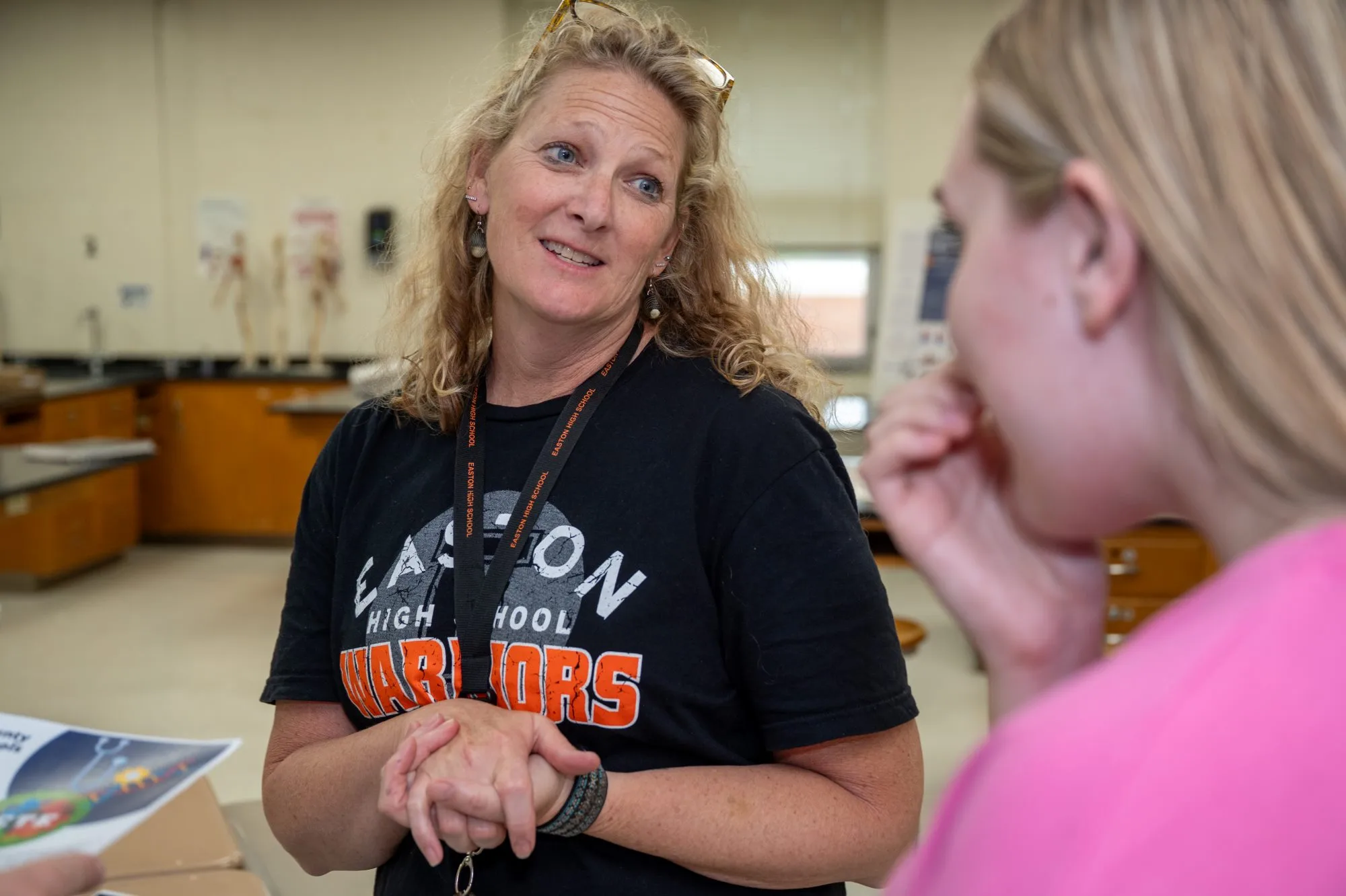 Woman in a black Easton High School Warriors shirt talks with a student in pink.