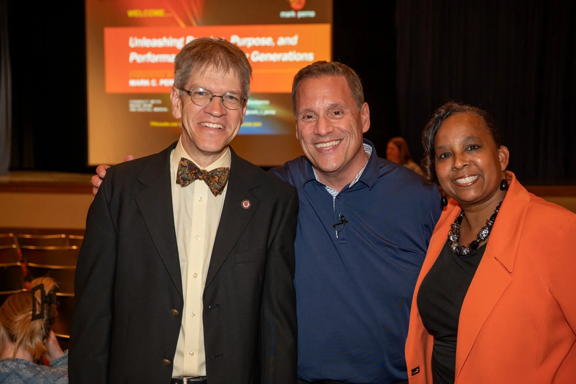 Three smiling people pose before a slide with orange title text about unleashing purpose and performance.