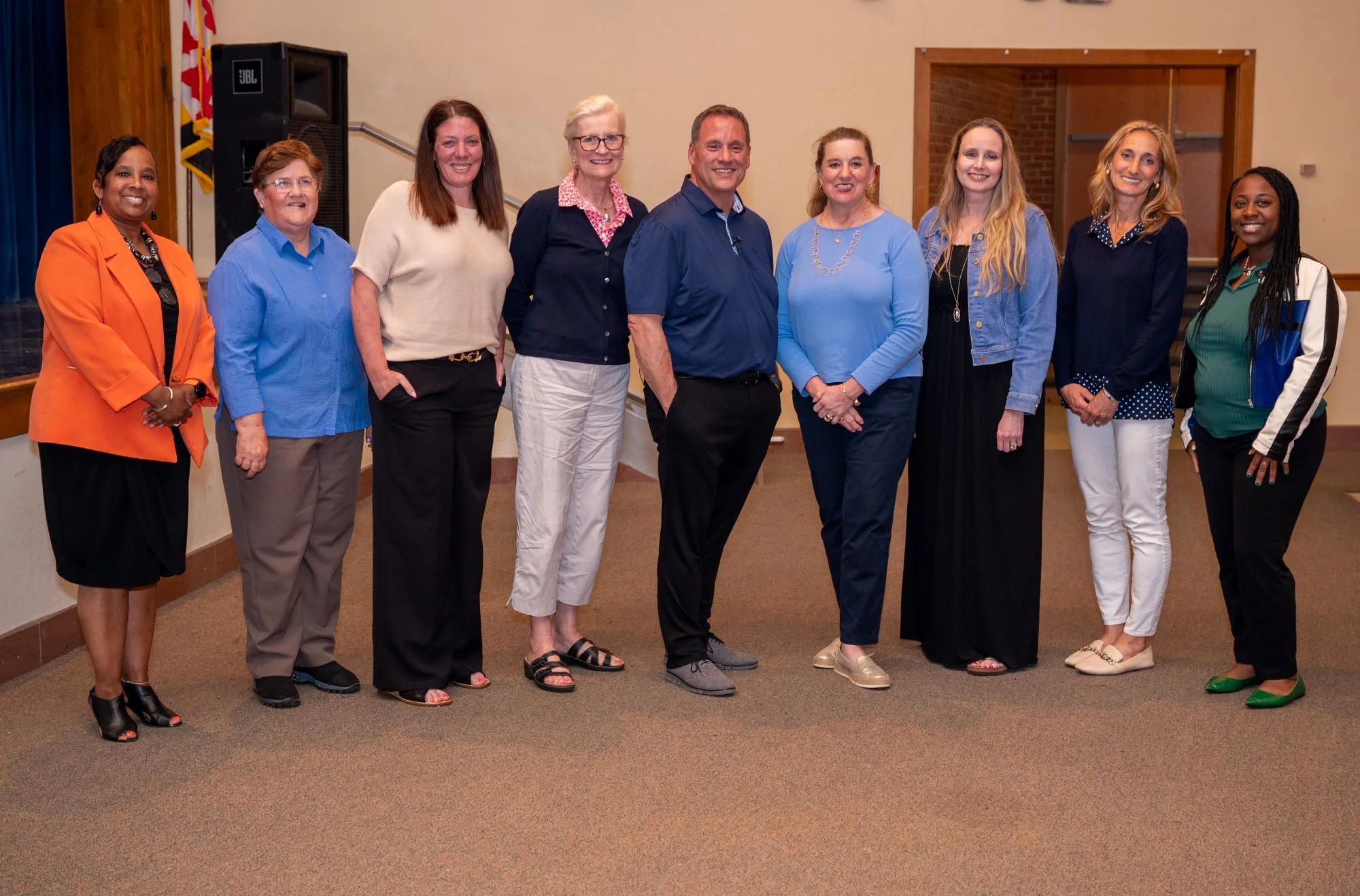 Nine people stand smiling in a row in an auditorium.