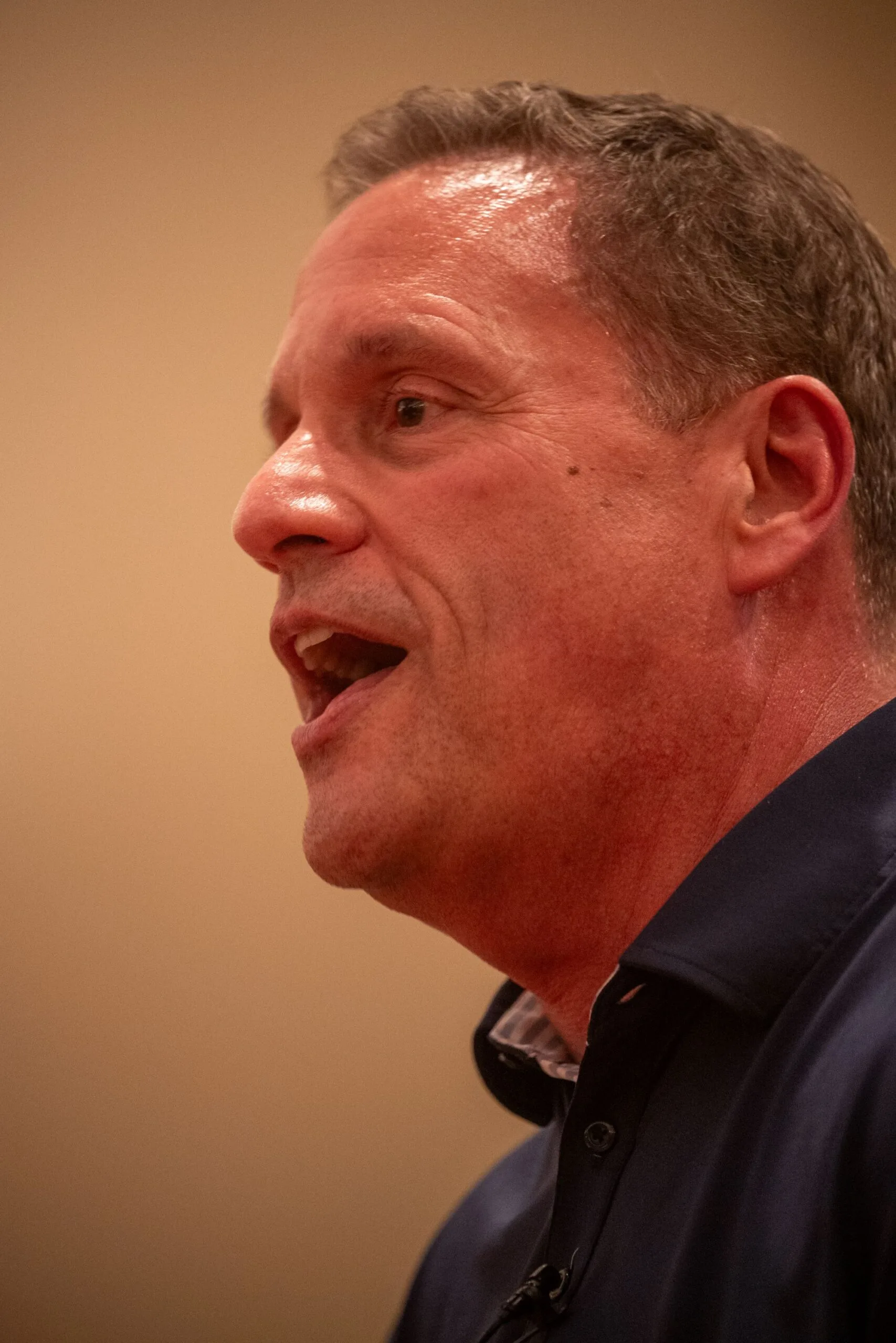 Close-up side profile of a speaking man in a navy shirt