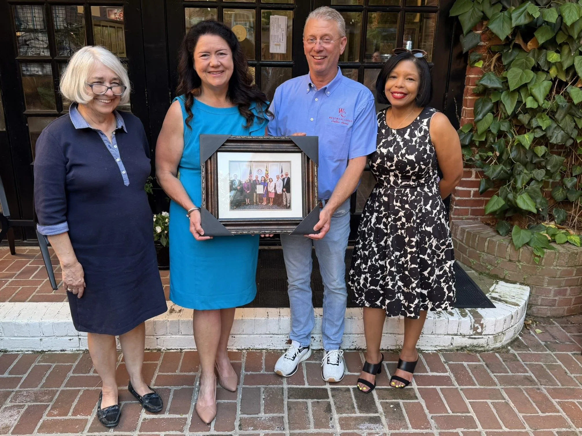 Four people in front of a dark doorway holding a framed photo of a certificate presentation